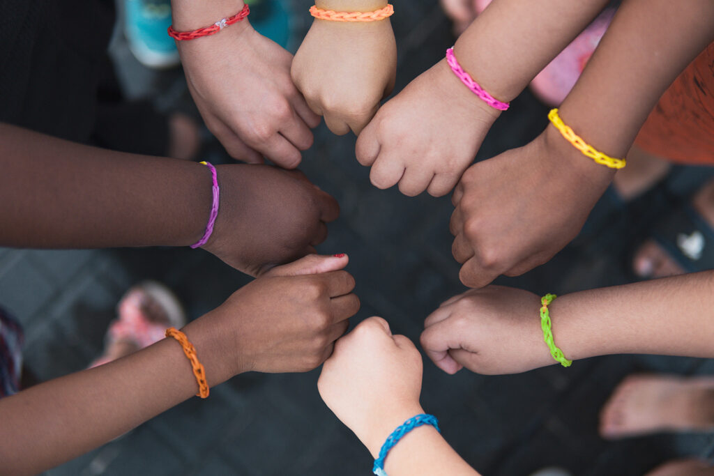 kids hands in a circle, all wearing rainbow bracelets